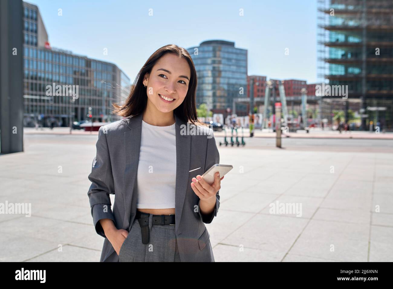 La giovane donna asiatica d'affari indossa il vestito in piedi sulla strada della città usando il telefono. Foto Stock