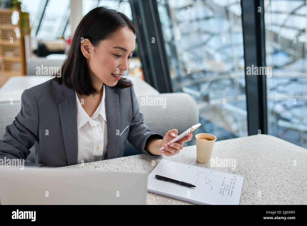 Giovane donna asiatica d'affari che indossa il vestito che lavora in ufficio usando il telefono delle cellule. Foto Stock