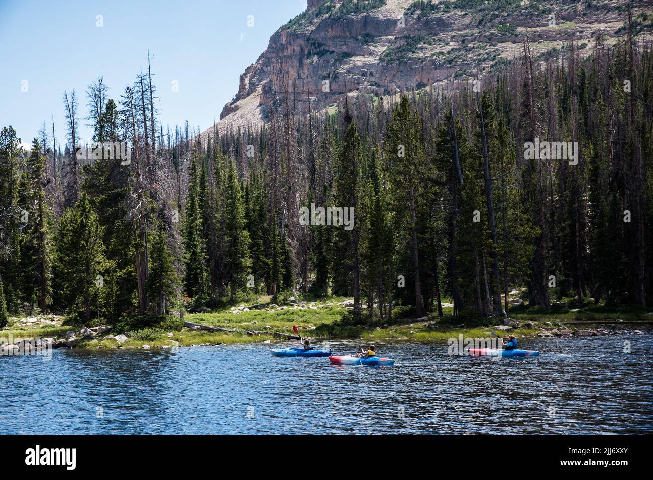 Tre kayak colorati in un lago di alta montagna. Le aspre montagne e la foresta forniscono il contesto alla scena. Foto Stock