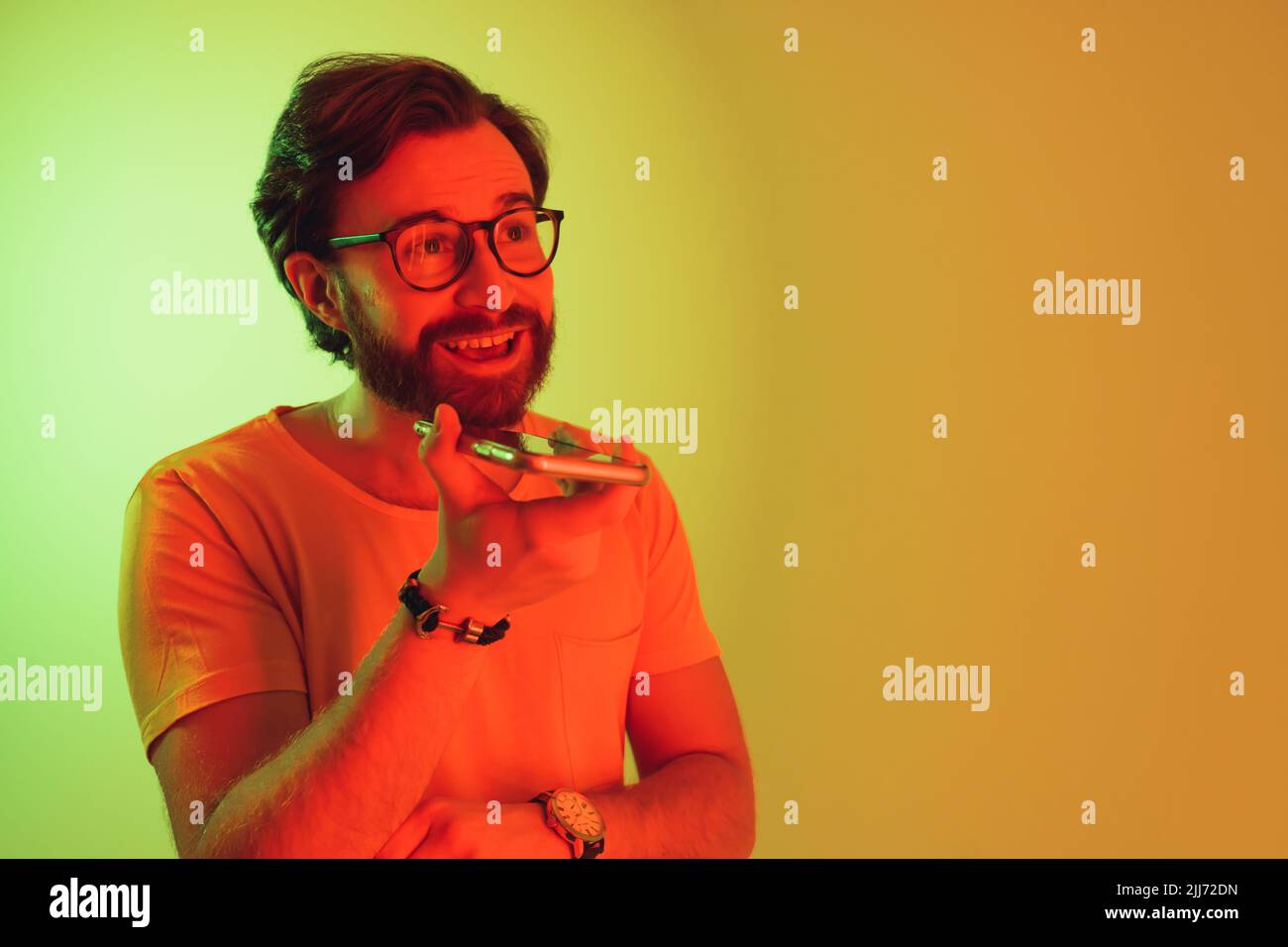 Giovane uomo elegante con barba che parla sullo smartphone in un ambiente da studio, con luci colorate . Foto di alta qualità Foto Stock