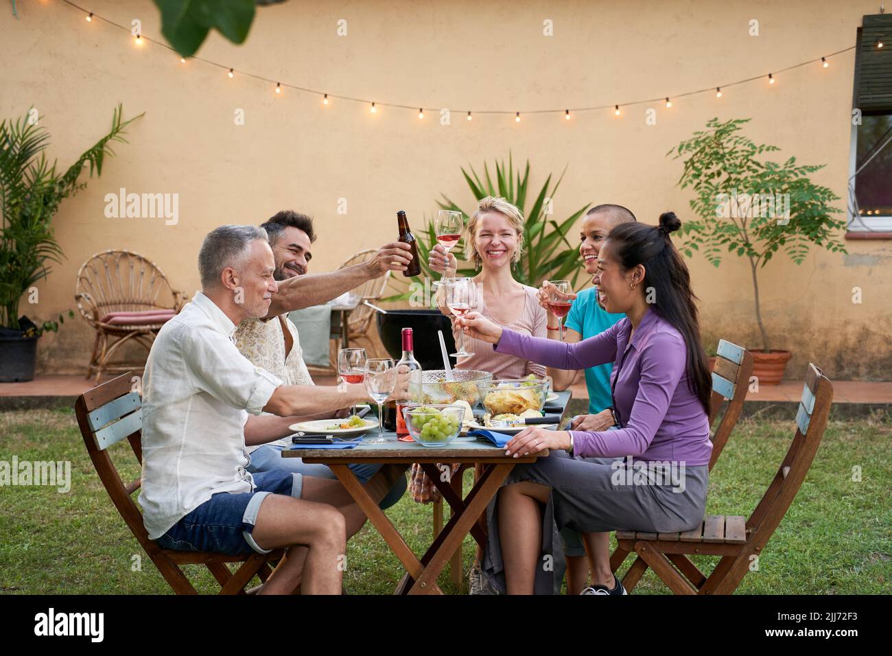 Famiglia felice mangiare e bere vino rosso a cena barbecue party all'aperto. Persone mature e giovani che mangiano insieme sul cortile. Giovani e anziani Foto Stock