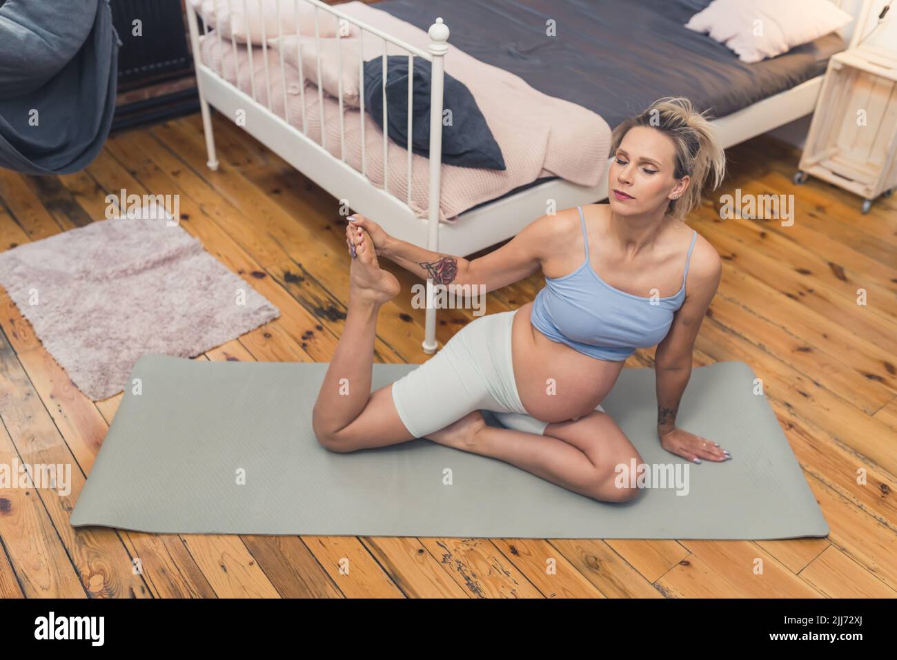 Esercizi di respirazione e stretching per le donne incinte. Giovane presto-to-mom seduta su un tappeto di yoga con e tenendo una delle sue gambe in su mentre respira tranquillamente. Concetto di gravidanza attiva. Foto di alta qualità Foto Stock