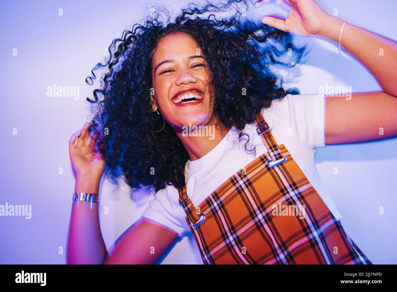 Giovane donna che balla e frusta i capelli felicemente. Ragazza allegra che ride gioiosamente mentre si alza da sola in una luminosa luce al neon. Spensierato giovane WO Foto Stock