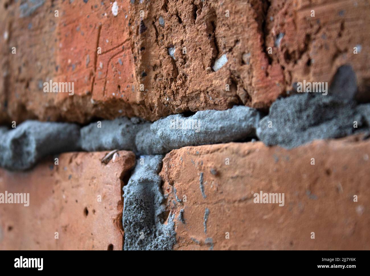 Primo piano della parete grezza grigia del mattone con fuoco selettivo del cemento Foto Stock