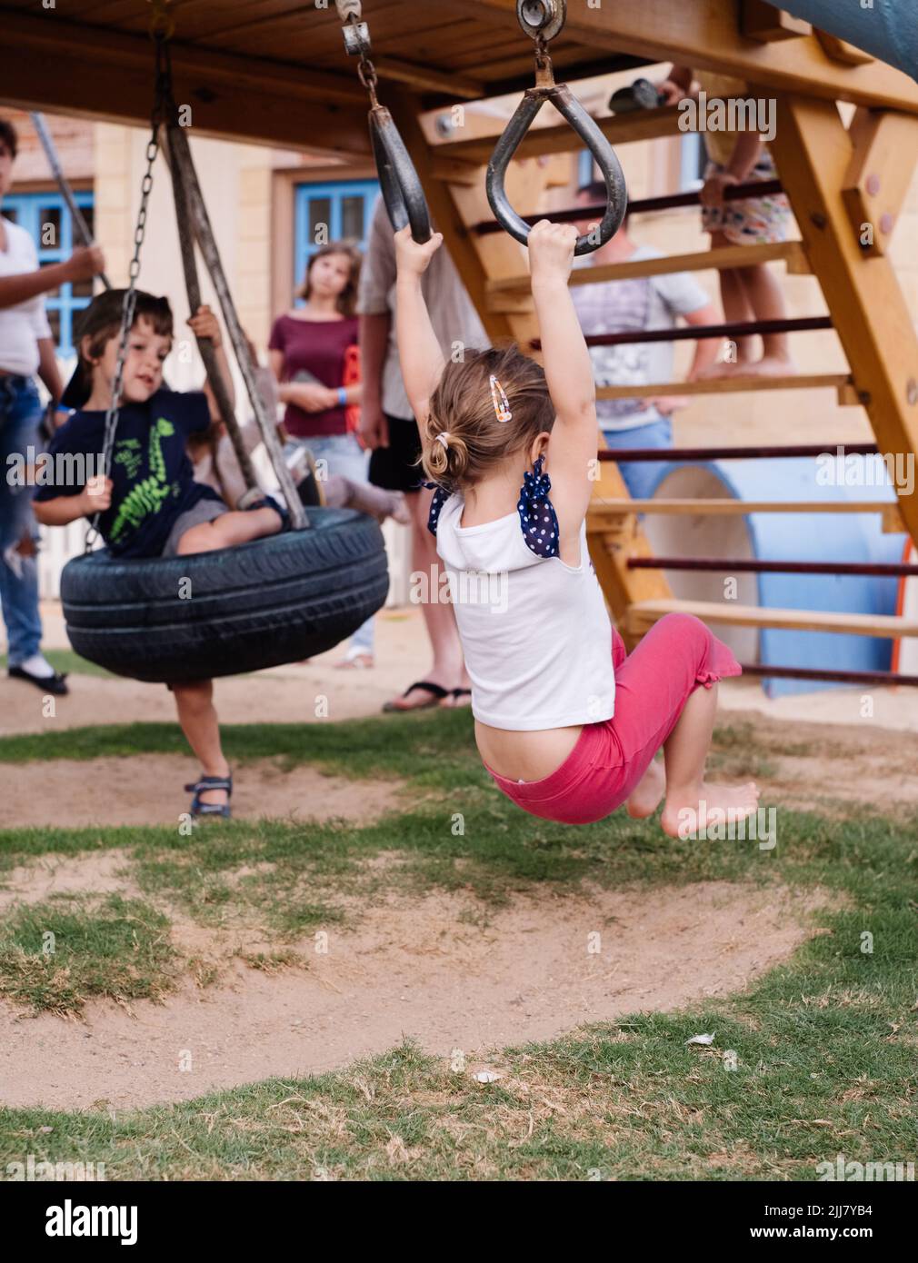Bambini che oscillano sugli anelli, oscillano dalle ruote sul parco giochi. Ragazza che si diverte durante la passeggiata. Forte, sportivo e piedi in estate Foto Stock