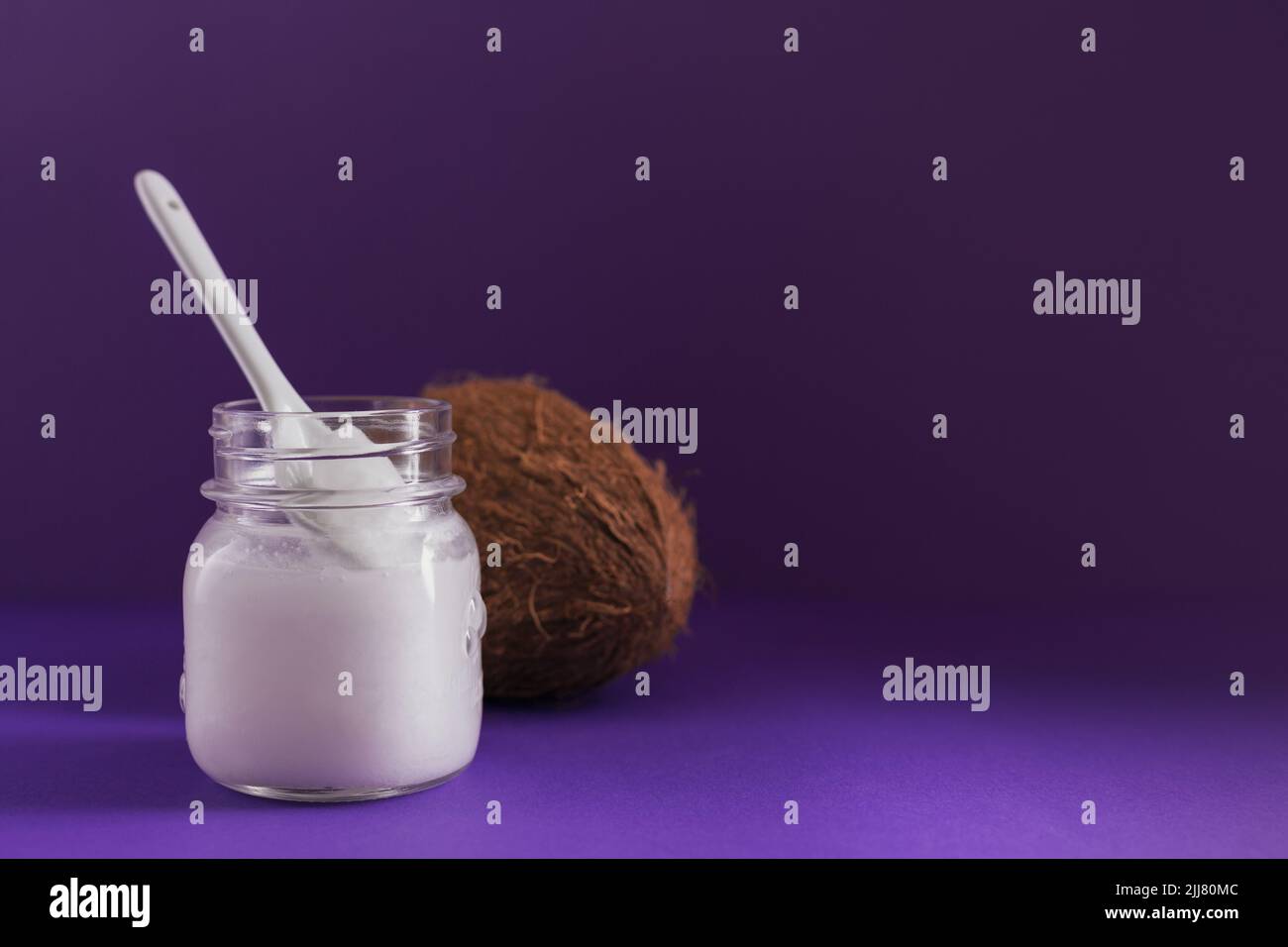 Cocco, fiocchi e olio di cocco in vaso su sfondo viola. Concetto di cucina sana Foto Stock