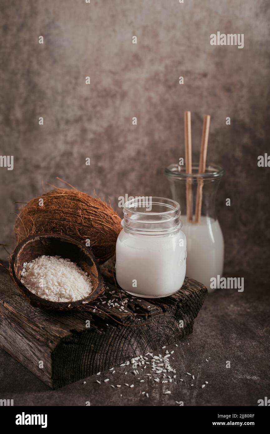 Bottiglia di latte vegano di cocco, olio di cocco, cocco intero e fiocchi su sfondo scuro Foto Stock
