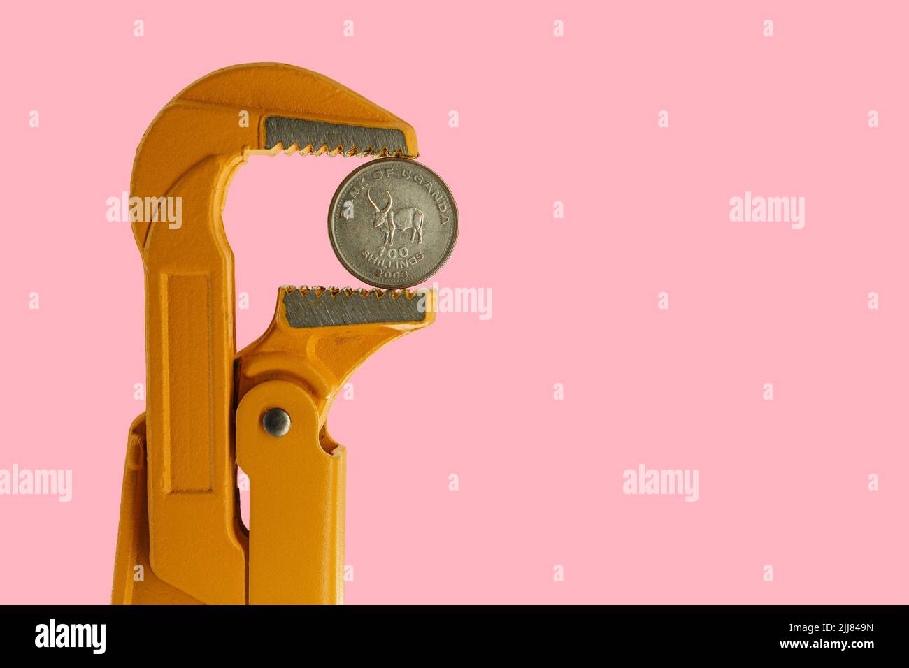 Cento scellini di moneta ugandese tenuti in una chiave per idraulico arancione su sfondo rosa Foto Stock