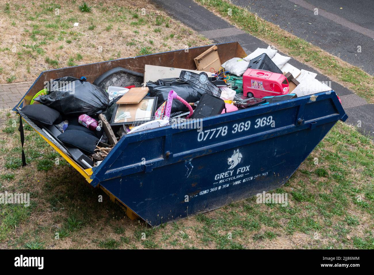 Un salto pieno di spazzatura domestica su un prato anteriore, Regno Unito Foto Stock