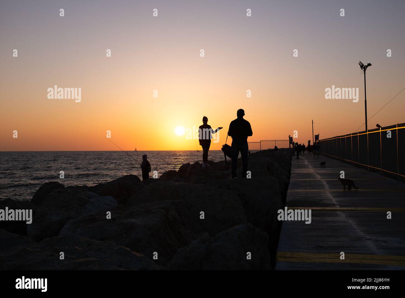 Silhouette di persone su un molo di mare durante il tramonto. Foto Stock