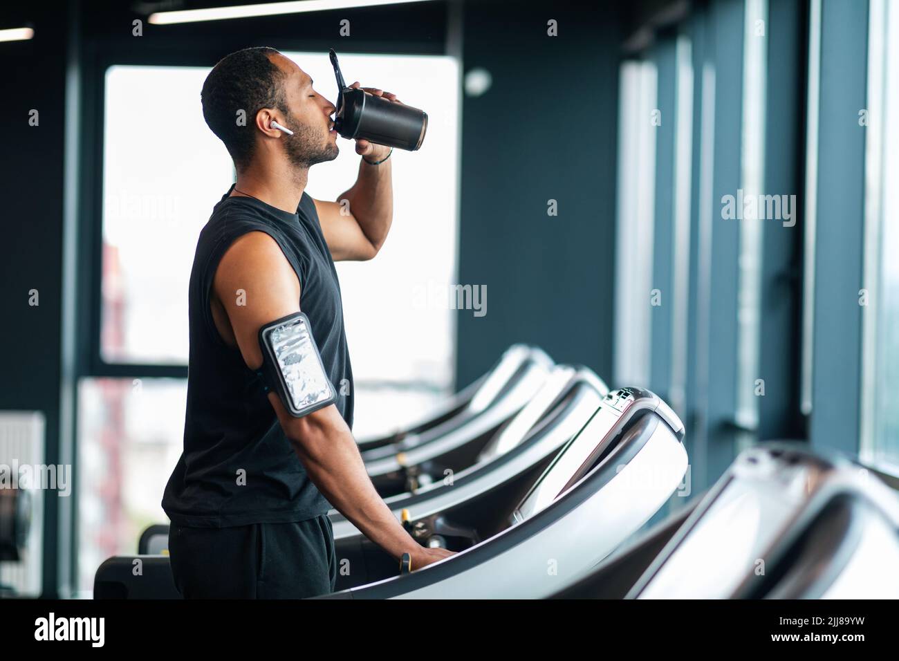 Bell'atleta maschio nero bere acqua mentre si allenano al tapis roulant in palestra Foto Stock