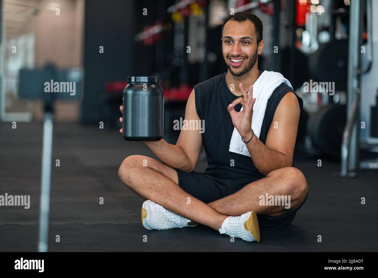 Bella atleta maschio nera che fa video revisione per polvere di siero in palestra Foto Stock