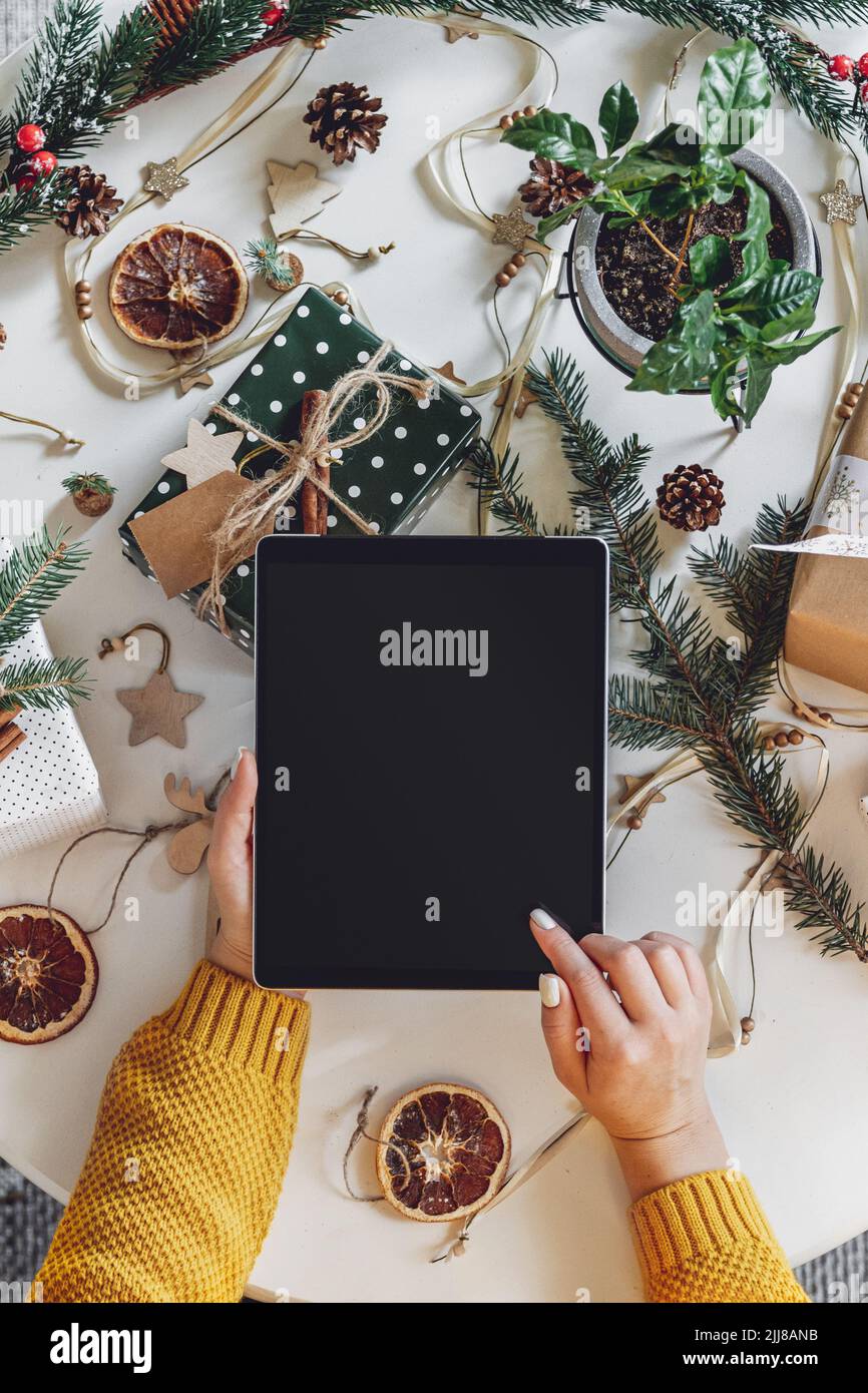 Mani femminili con tablet sul tavolo con decorazioni natalizie fatte a mano Foto Stock