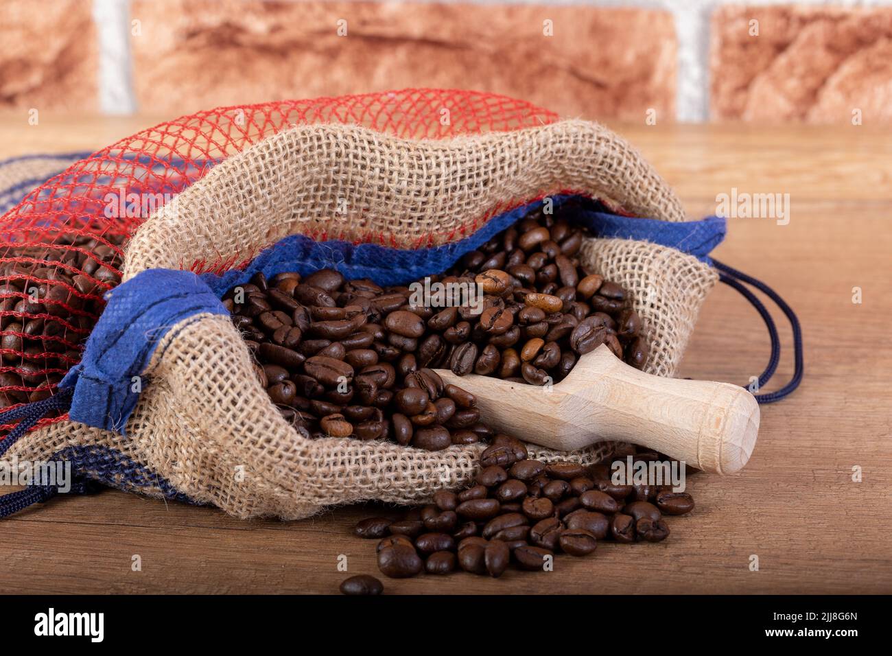 Chicchi di caffè nero arrostiti con un cucchiaio di legno, fuoriuscite dal sacco sul tavolo. Foto per una caffetteria, un caffè o un ristorante. Foto Stock