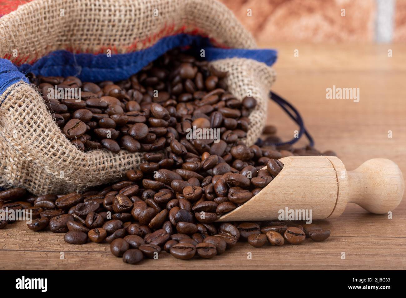 Chicchi di caffè nero arrostiti con un cucchiaio di legno, fuoriuscite dal sacco sul tavolo. Foto per una caffetteria, un caffè o un ristorante. Foto Stock