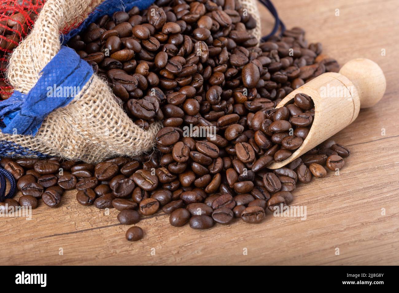 Chicchi di caffè nero arrostiti con un cucchiaio di legno, fuoriuscite dal sacco sul tavolo. Foto per una caffetteria, un caffè o un ristorante. Foto Stock