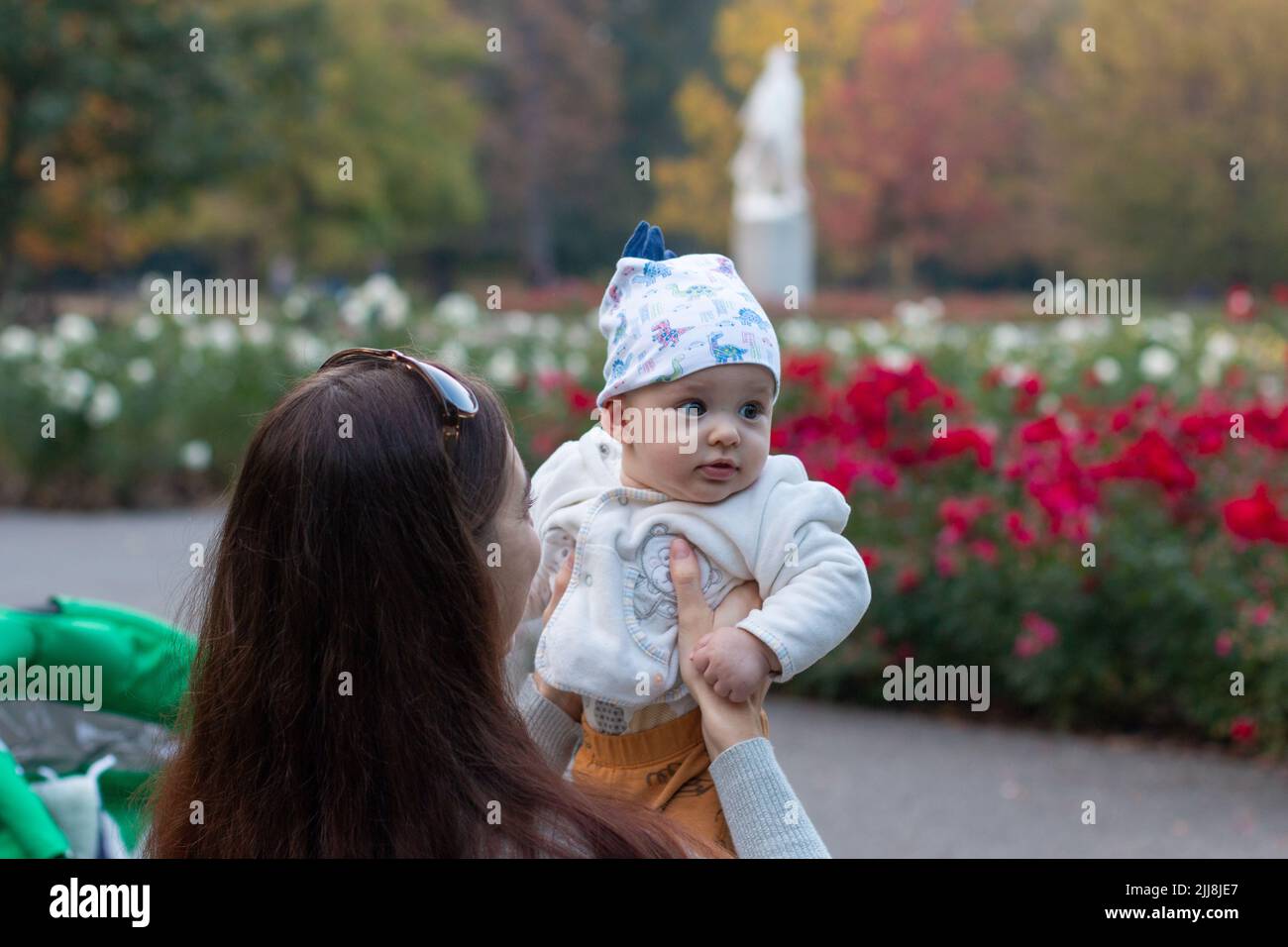 Madre che tiene il bambino carino in mani all'aperto al parco del giardino dei fiori, sfondo della natura d'autunno Foto Stock