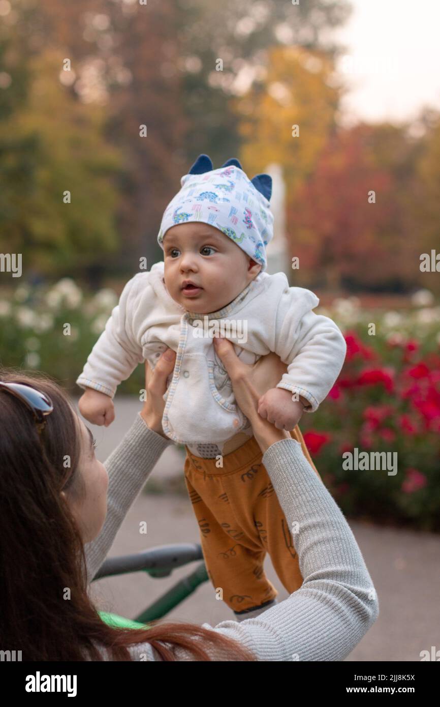 Madre che alza il bambino cute all'aperto nel parco del giardino dei fiori Foto Stock