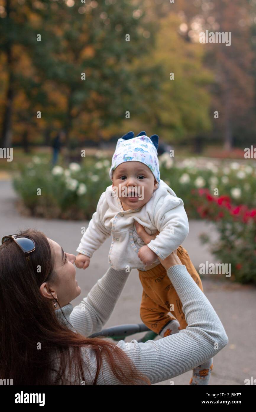 Giovane madre che raccoglie il bambino allegro nelle sue braccia fuori nel parco Foto Stock