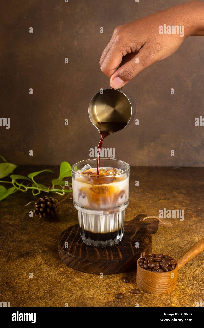 caffè ghiacciato con latte condensato su montagne russe rustiche in legno e con piante verdi, chicchi di caffè pieni su cucchiaino di legno d'annata in cima al vecchio sfondo rustico Foto Stock