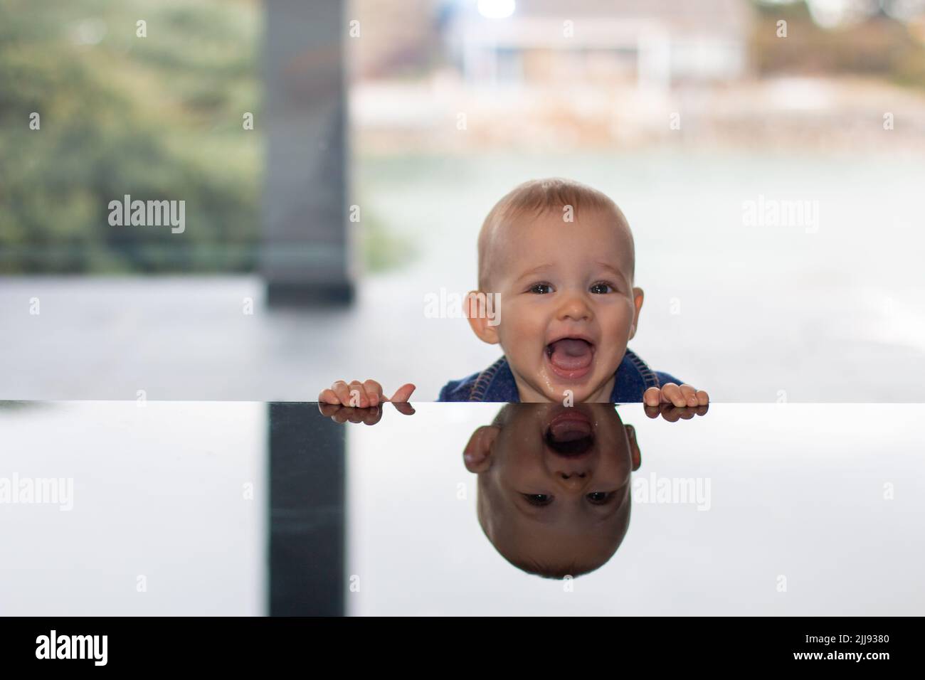 Ride carino naughty bambino ritratto con la testa sopra il tavolo di vetro con riflessione, bambino positivo casa vita concetto scena Foto Stock