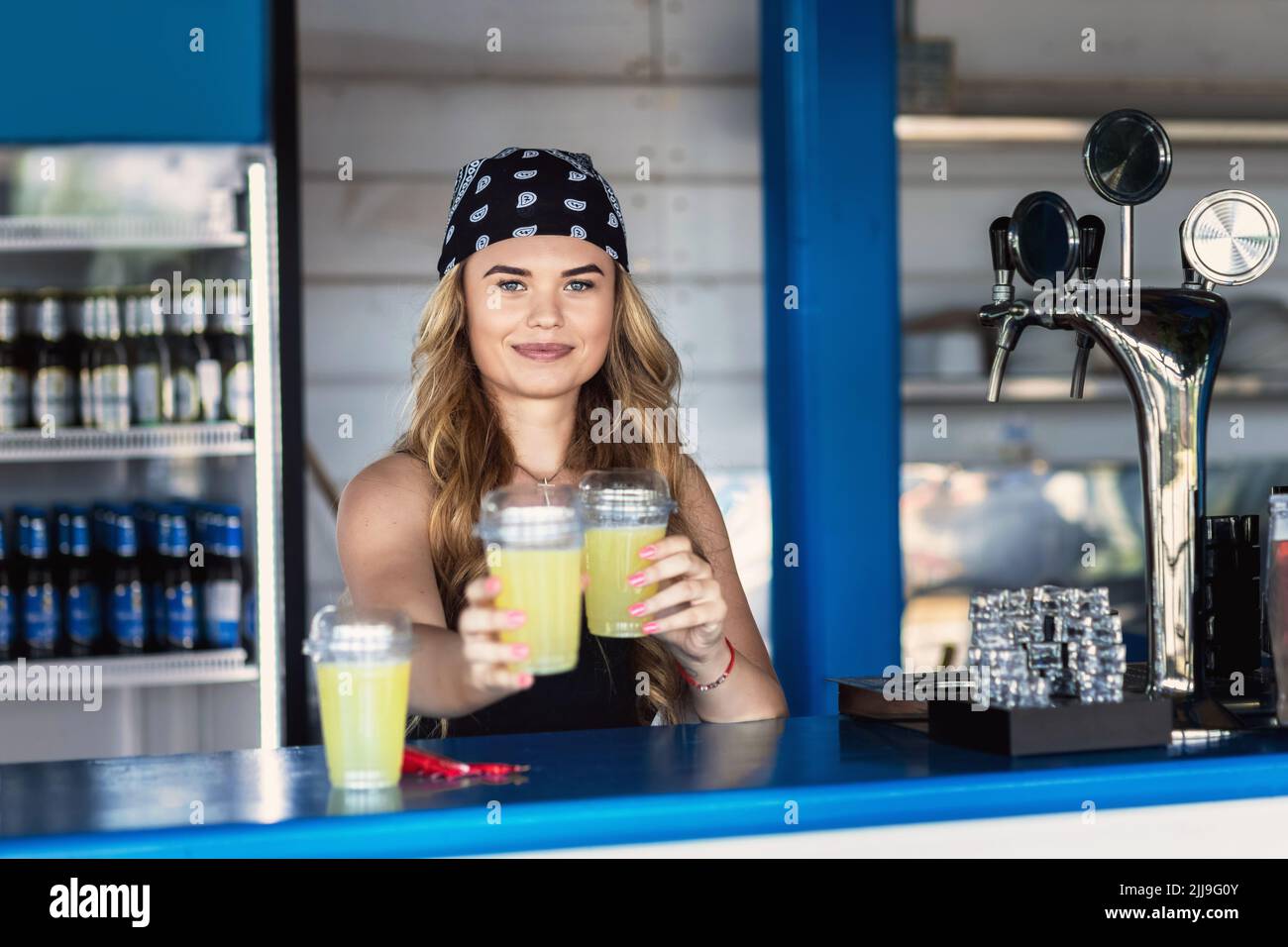 Barman ragazza hipster che serve limonata fresca dietro il bancone al bar all'aperto durante il festival estivo Foto Stock