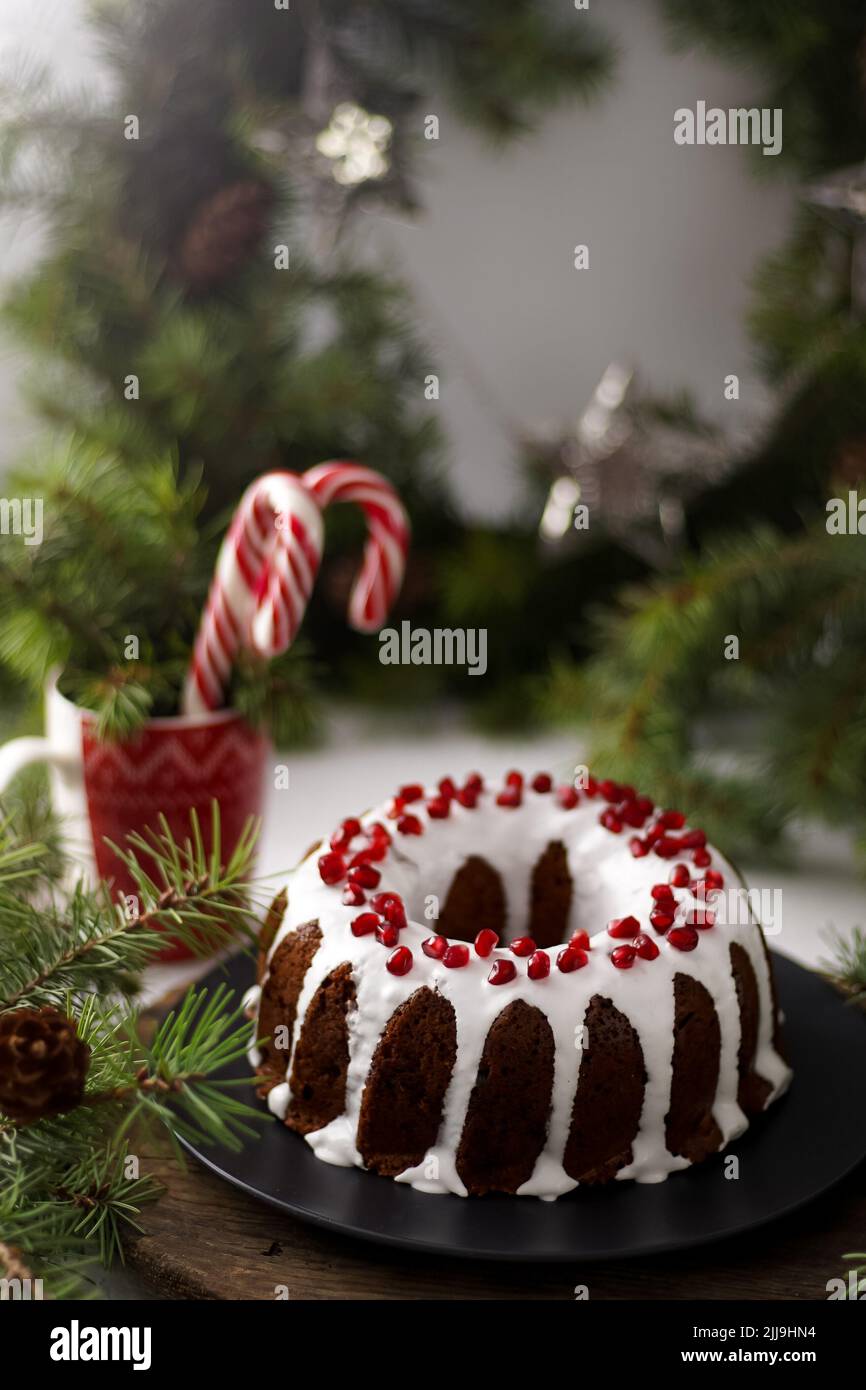 Cibo di Natale. Torta rotonda con glassa bianca. Cupcake con buco al centro con melograno. Rami di abete rosso verde sul tavolo. Vita morta. Dolci, dolci e dolci per il nuovo anno. Foto Stock