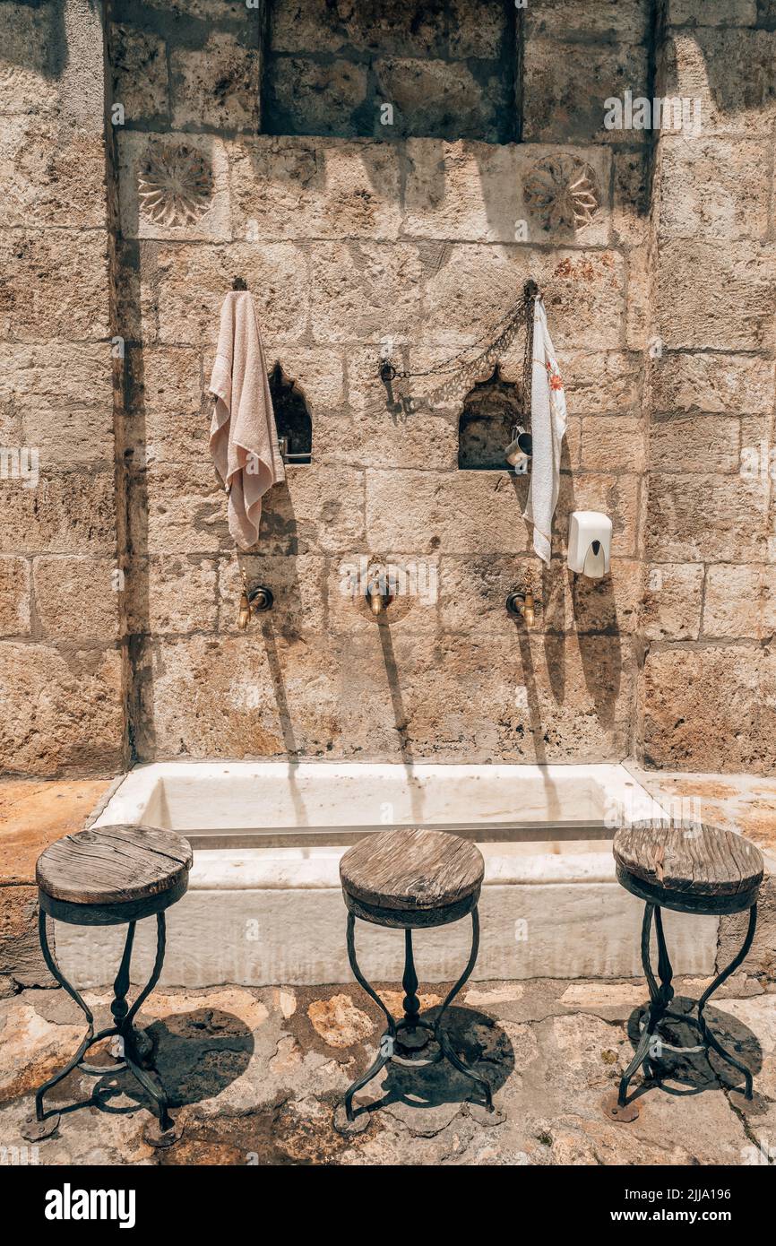 Rubinetti d'acqua e sedili in legno utilizzati per l'ablazione rituale islamica in moschea Foto Stock