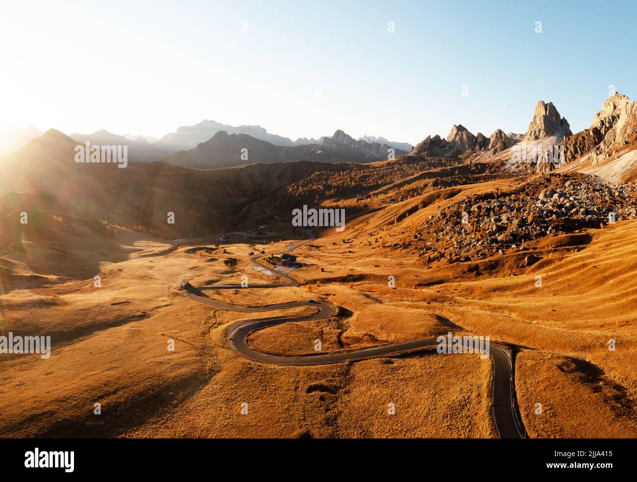 Pittoresca vista aerea su strada tortuosa in autunno valle di montagna al tramonto. La luce dorata del tramonto illumina le montagne e l'erba arancione. Passo Giau, Alpi dolomitiche, Dolomiti, Italia Foto Stock