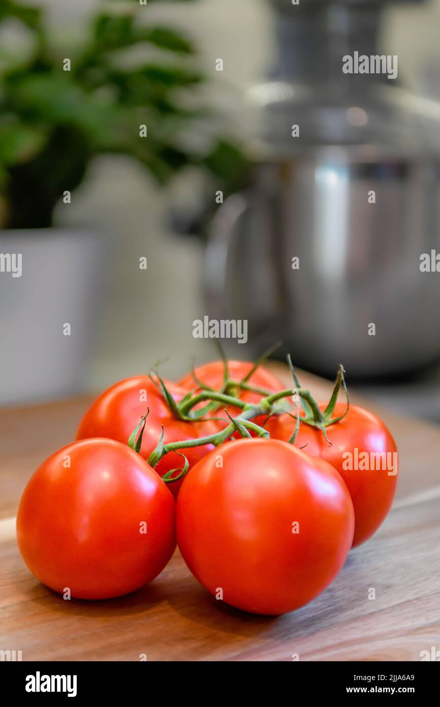 Pomodori rossi su vite in cucina - pomodori freschi a fette e integrali su tagliere di legno - grappolo e grappolo Solanum lycopersicum maturi Foto Stock