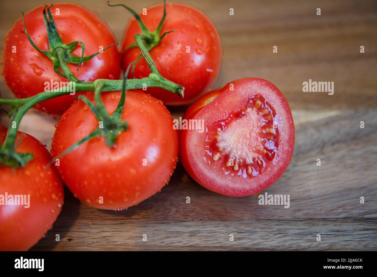 Pomodori rossi su vite in cucina - pomodori freschi a fette e integrali su tagliere di legno - grappolo e grappolo Solanum lycopersicum maturi Foto Stock
