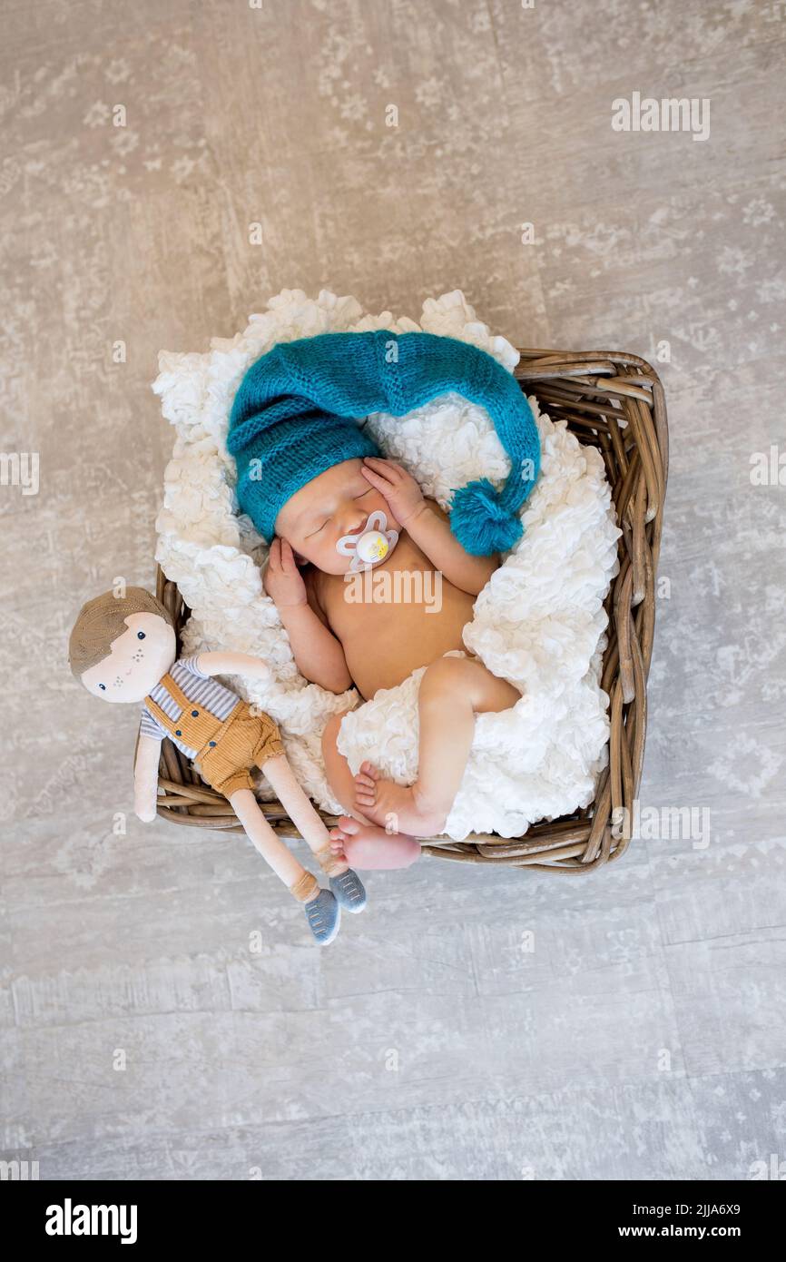 Un bambino neonato in un cappello di maglia blu dorme tranquillamente con un giocattolo in un cestino Foto Stock