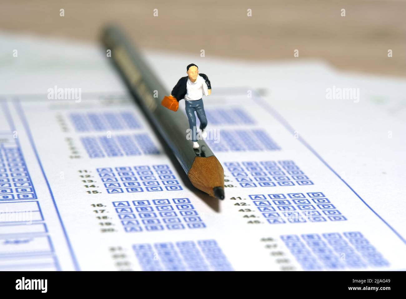 Fotografia di personaggi giocattolo in miniatura. Concetto del giorno dell'esame in ritardo. Uomini pupilla che corre sopra la matita e foglio di carta di risposta di esame. Immagine pho Foto Stock