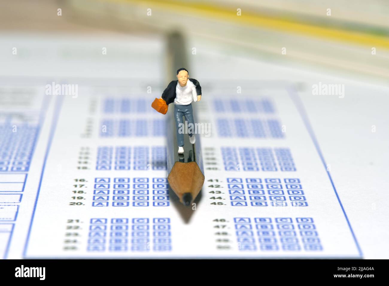 Fotografia di personaggi giocattolo in miniatura. Concetto del giorno dell'esame in ritardo. Uomini pupilla che corre sopra la matita e foglio di carta di risposta di esame. Immagine pho Foto Stock