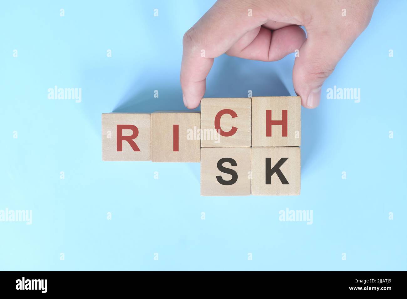 Rischio per un concetto aziendale ricco. Parole cambianti a mano su blocchi di legno su sfondo blu. Foto Stock