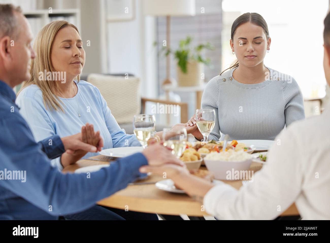 Siate grati, sempre. Una bella famiglia che benedica il cibo con una preghiera a tavola insieme a casa. Foto Stock