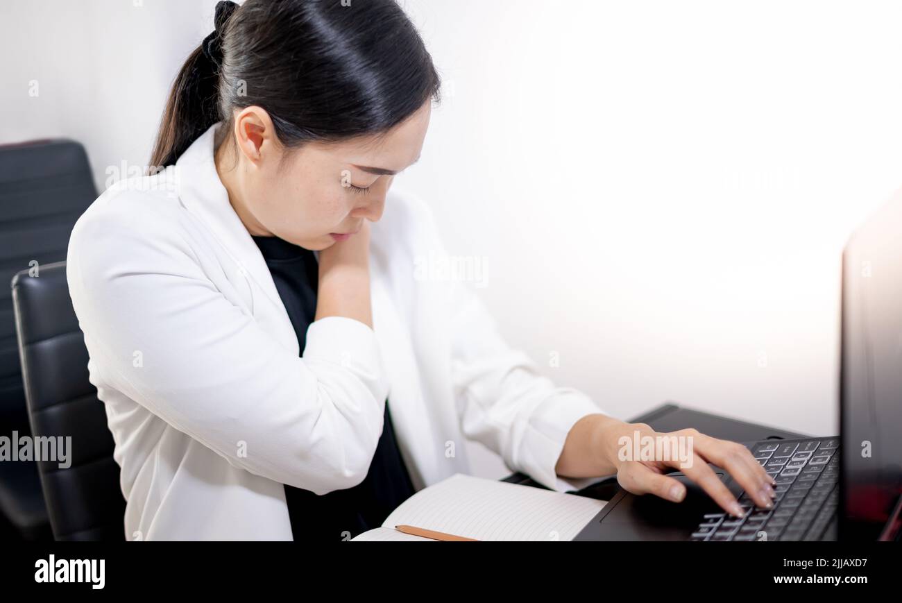 I giovani asiatici sentono dolore dal lavoro, mentre si siedono di fronte a un computer portatile nella loro casa. Concetto di sindrome da ufficio della donna che lavora. Foto Stock