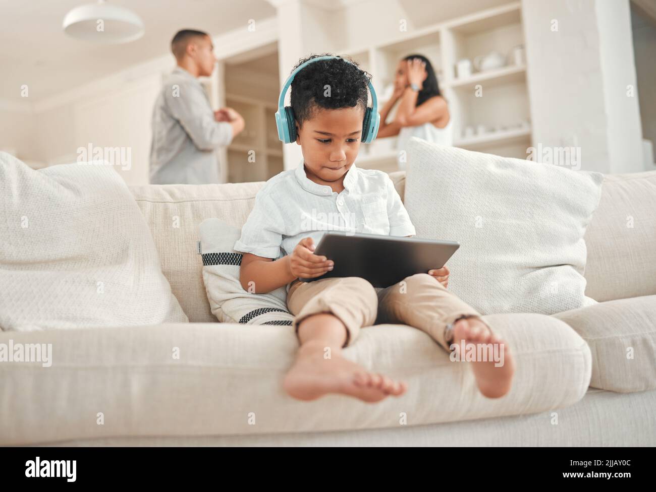 Hai fallito la tua famiglia. Un ragazzino che indossa una cuffia e usa un tablet digitale mentre i genitori discutono in background a casa. Foto Stock