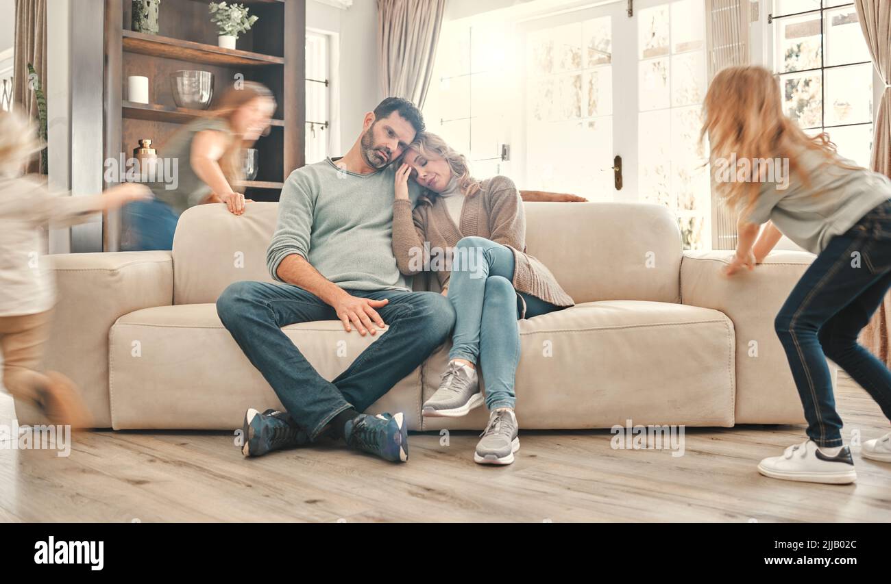 Ci sarà mai una pausa: Due genitori si sono esauriti sul divano mentre i bambini giocano a casa. Foto Stock