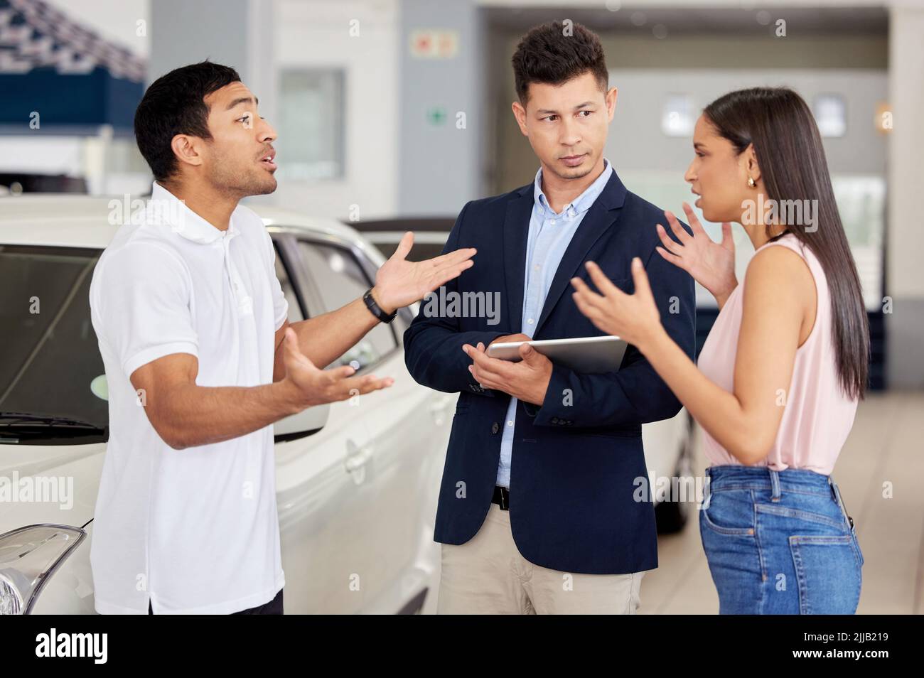 Scegliere un'auto non è mai una decisione facile. Una giovane coppia che ha un argomento davanti a un venditore di auto. Foto Stock