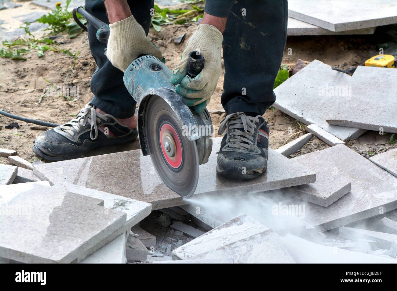 Un lavoratore con una sega circolare taglia una piastrella in primo piano. Foto Stock
