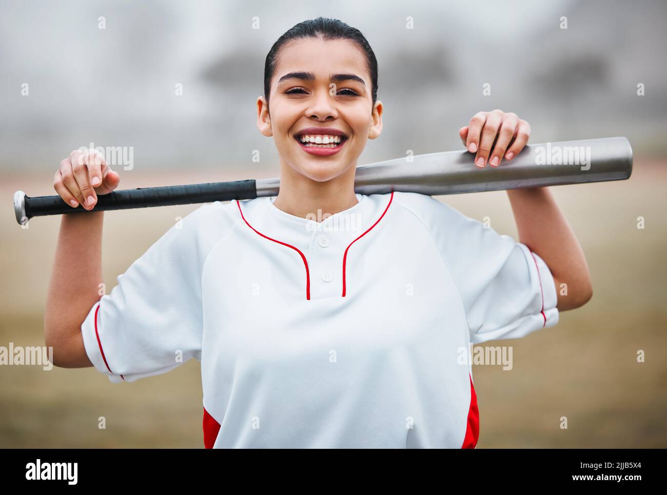 Pastella su. Ritratto ritagliato di un attraente giovane giocatore di baseball femminile in piedi all'esterno. Foto Stock