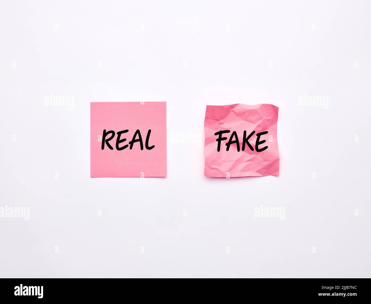 Le parole falso e reale su fogli rosa di carta di nota su sfondo bianco. Imitazione del prodotto o concetto di informazione genuina. Foto Stock