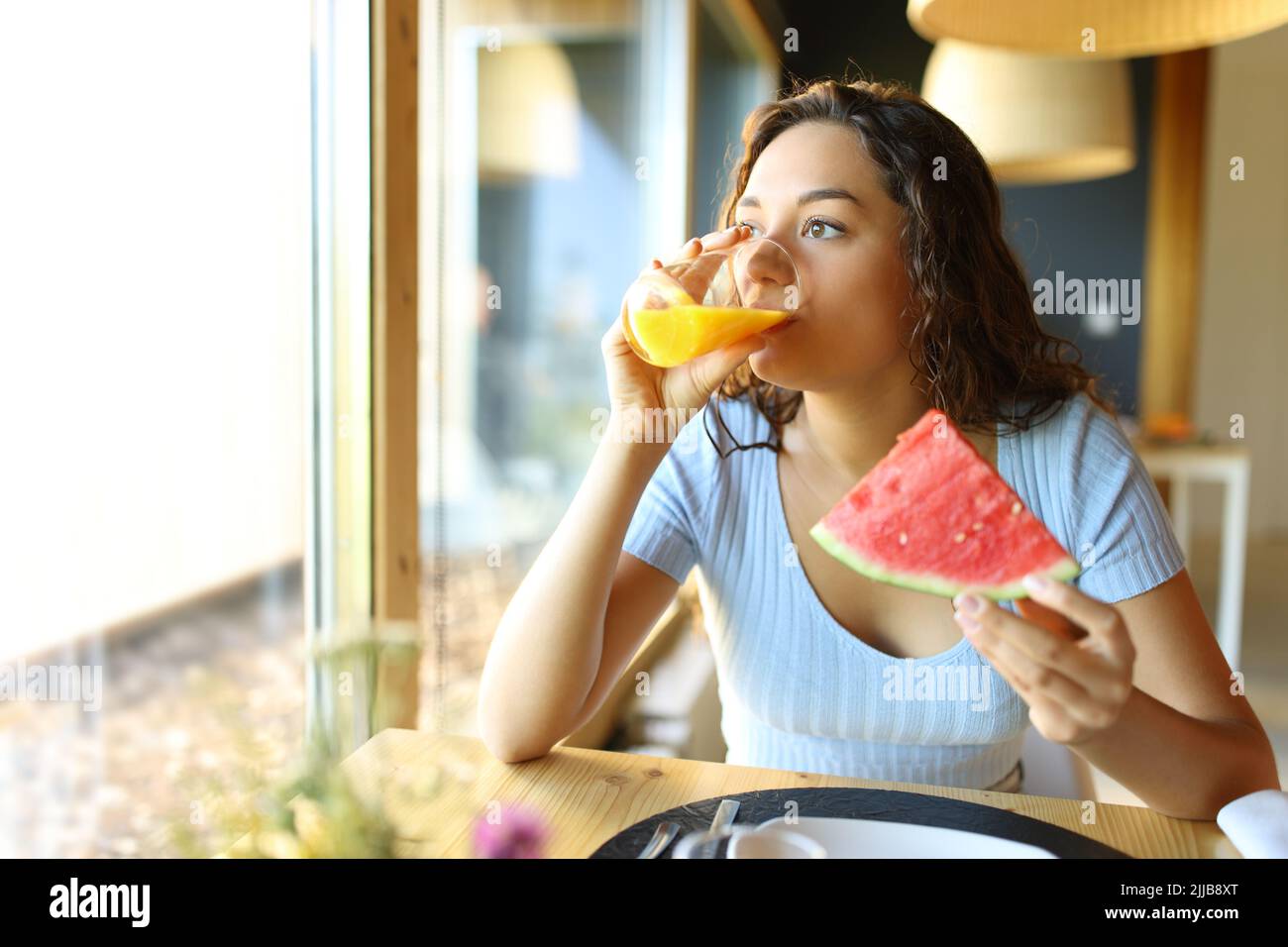 Donna che beve succo d'arancia e mangiare cocomero in un ristorante interno Foto Stock