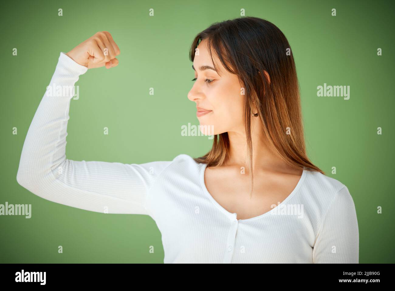 Sfide personali, crescita pubblica. Studio girato di una giovane donna che mostra il suo forte bicep su uno sfondo verde. Foto Stock