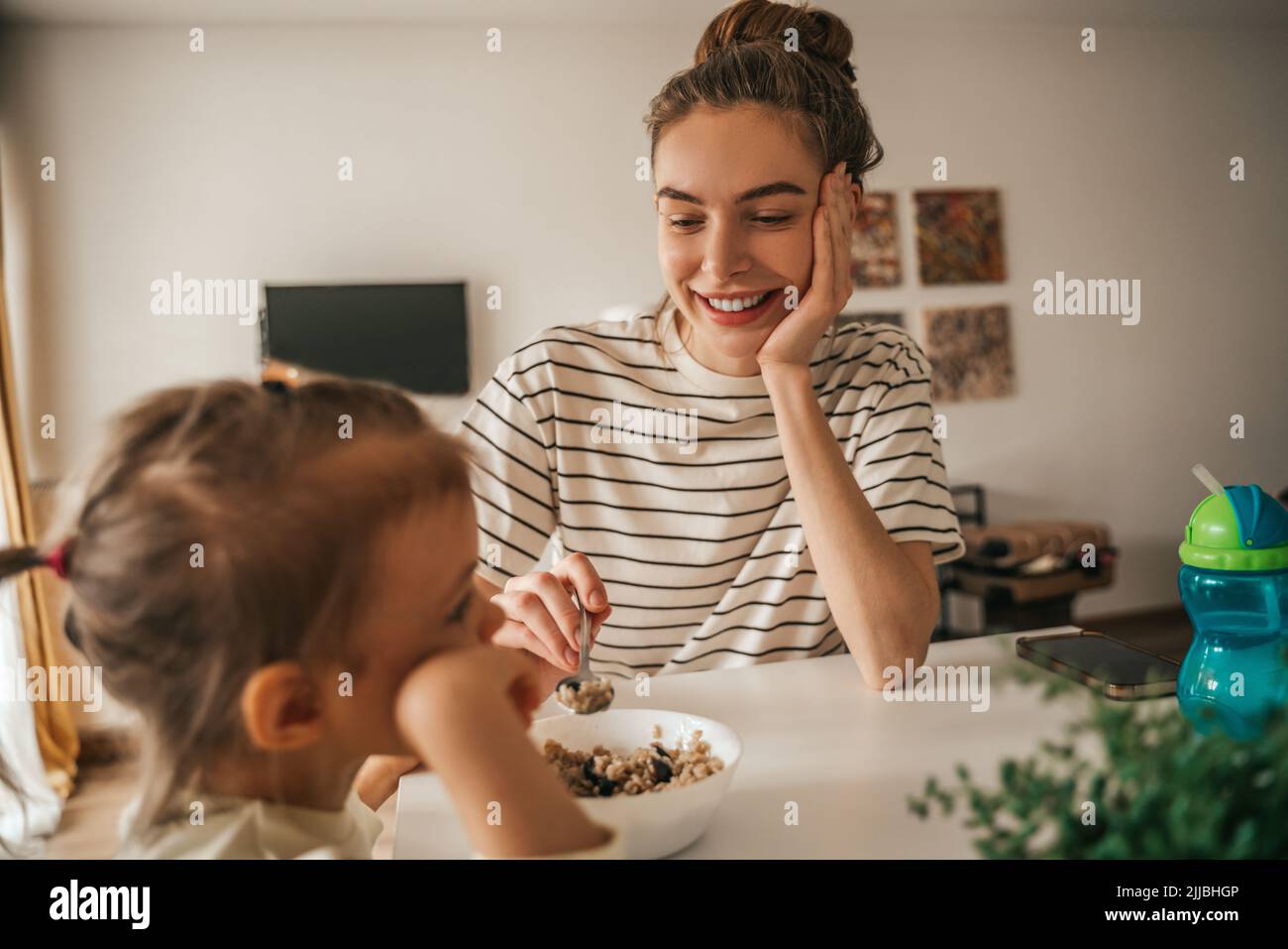 Femmina genitore che alimenta farina d'avena a sua figlia durante il mea di mattina Foto Stock