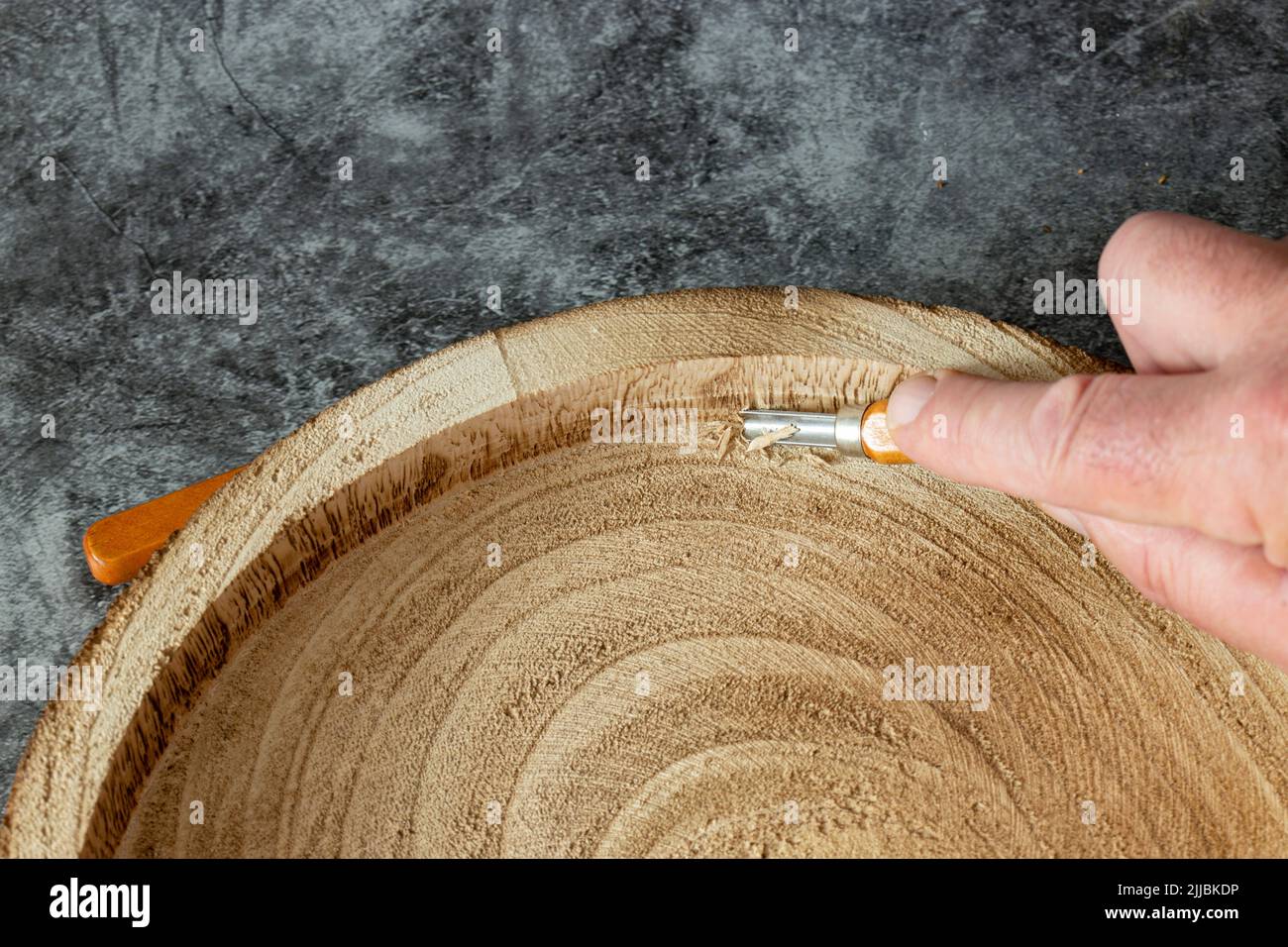 Uomo che intagliano un tronco di legno in una ciotola o in un piatto, con uno scalpello smussato. Su sfondo di pietra scura Foto Stock