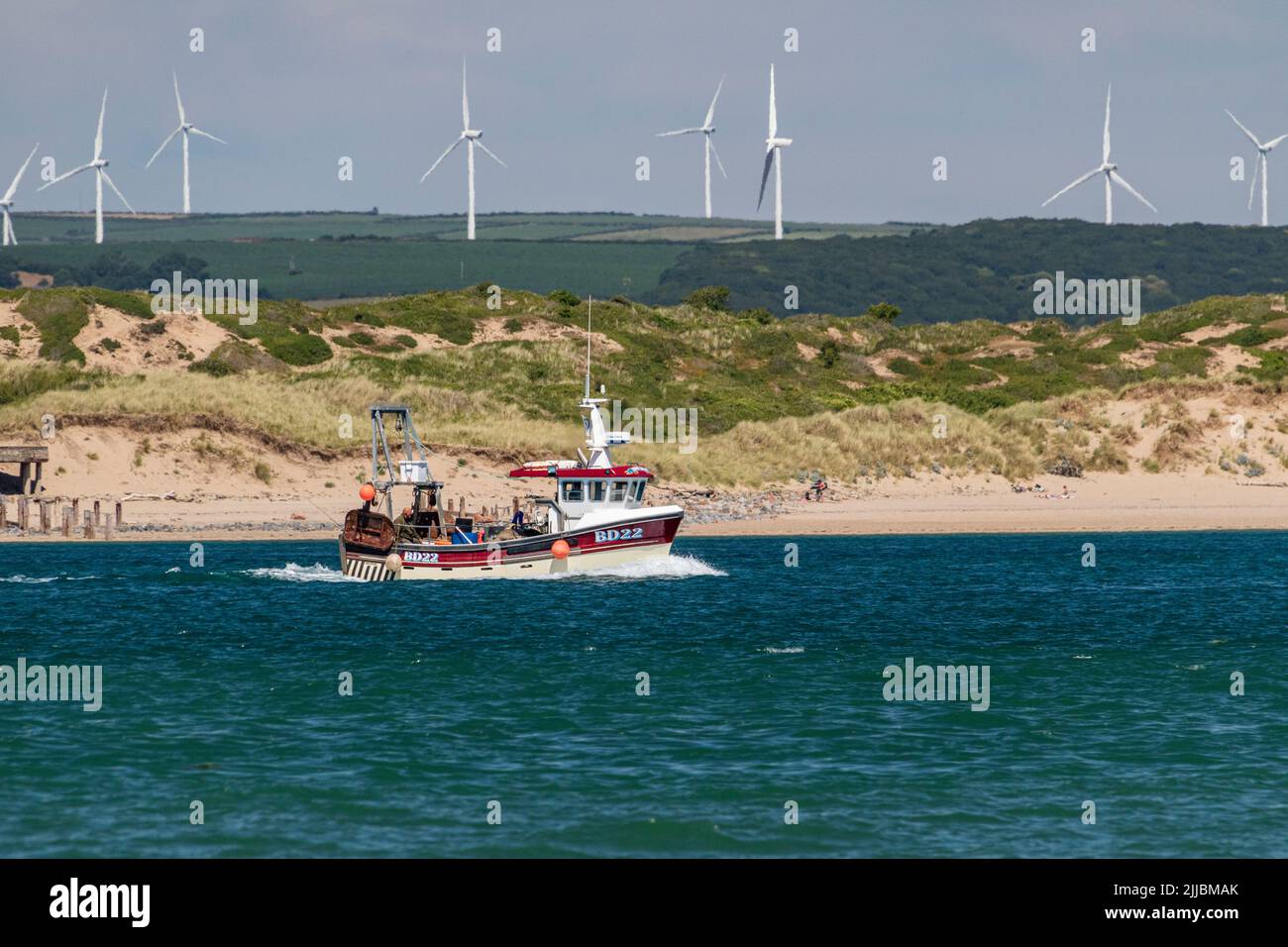 Barca da pesca di ritorno a Bideford su una marea in ascesa nell'estuario del Torridge di Taw con Burrows Braunton e turbine eoliche presso Fullabrook Farm. Foto Stock