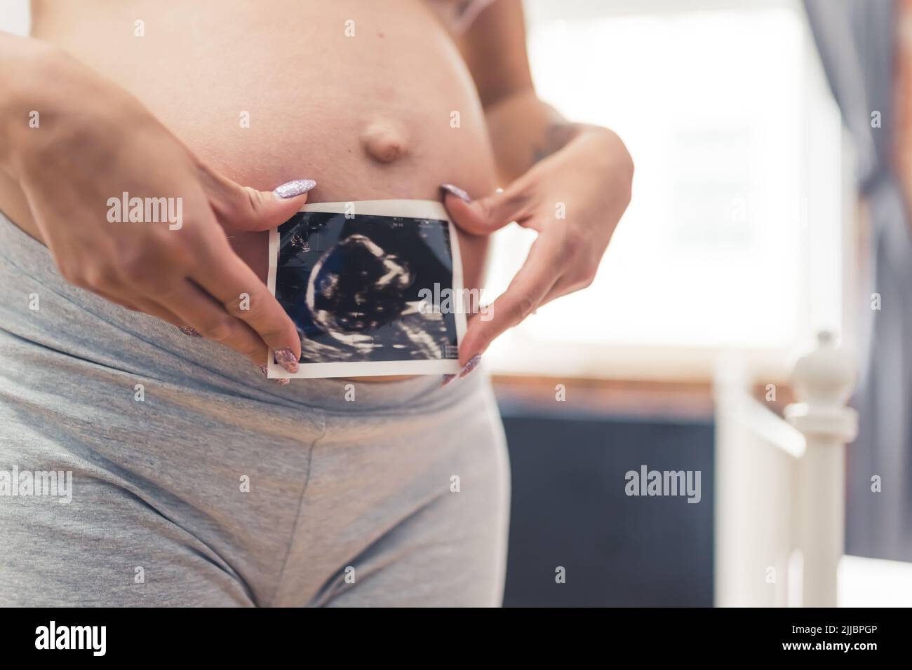 Ventre incinta di una persona caucasica in pantaloncini da motociclista grigi e una scansione della testa del suo nascituro. Concetto di genitorialità futura. Foto di alta qualità Foto Stock