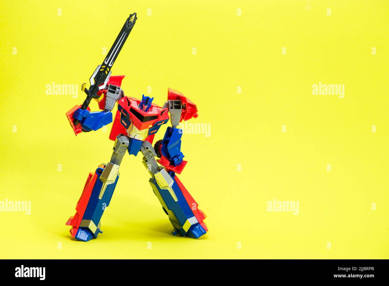 Trasformatore robot rosso e blu su sfondo giallo con spazio per il testo. Giocattoli per bambini, negozio di giocattoli. Foto Stock